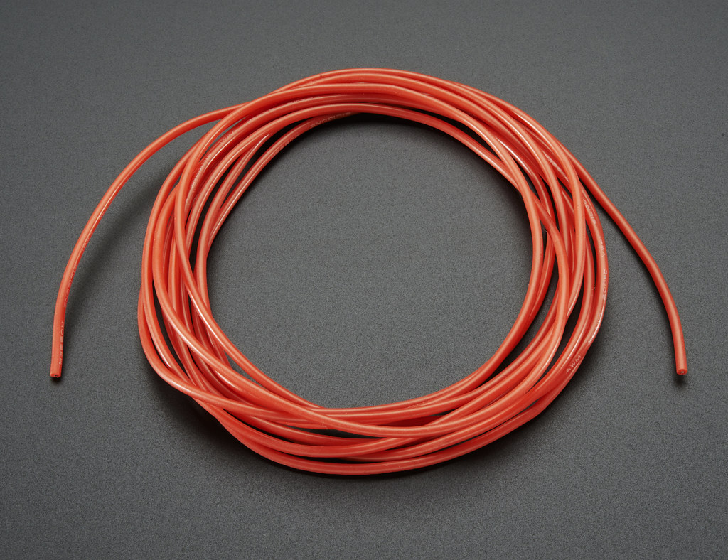 A wire with red, silicone insulation coiled up on a dark grey surface