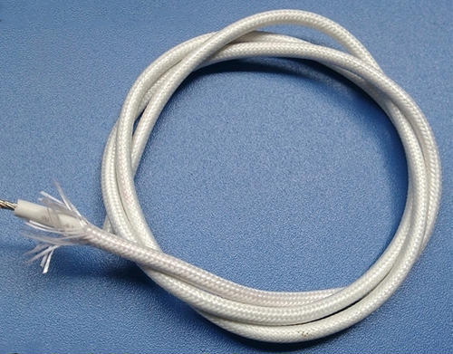 A fiberglass insulated cable with its end stripped, pictured over a grey surface